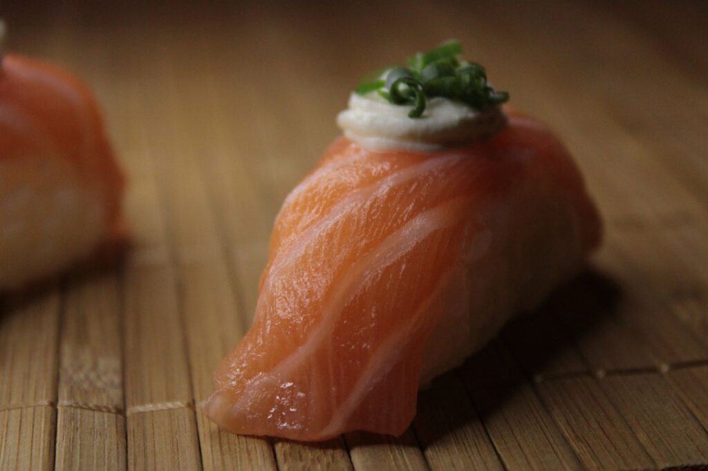 Délicieux sushi nigiri au saumon avec wasabi crémeux et oignons verts sur un tapis en bambou.