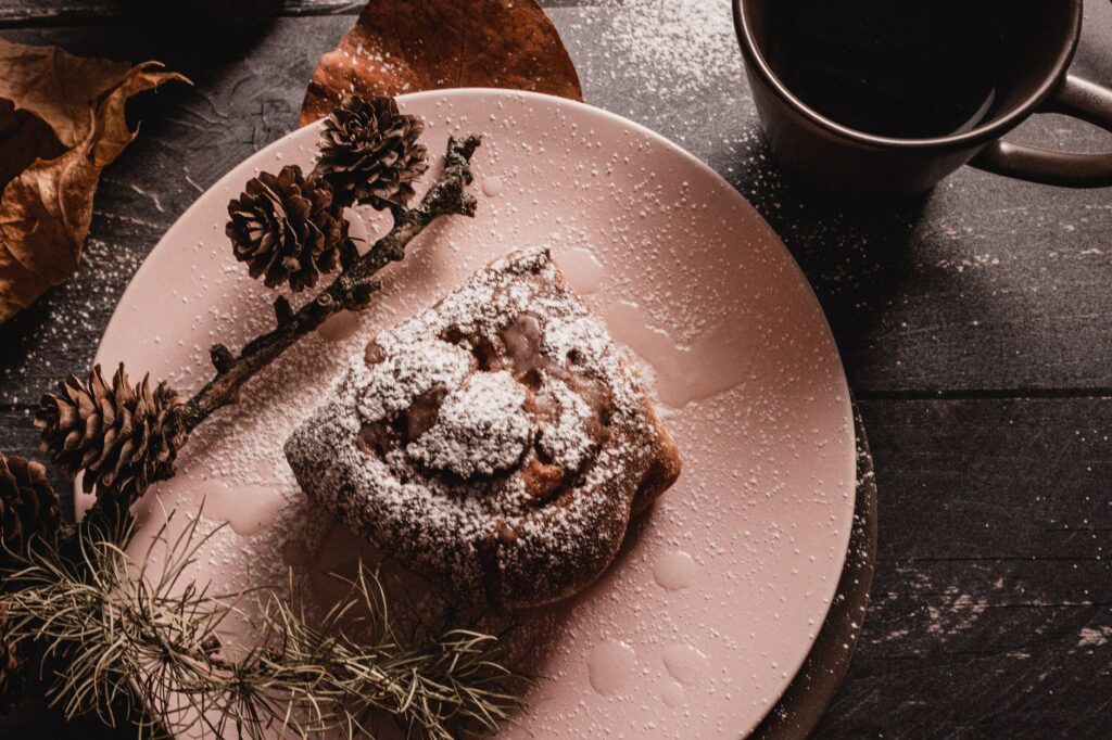 Brioches à la cannelle saupoudrées de sucre glace, servies avec du café et des pommes de pin sur une table rustique.