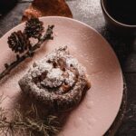 Brioches à la cannelle saupoudrées de sucre glace, servies avec du café et des pommes de pin sur une table rustique.