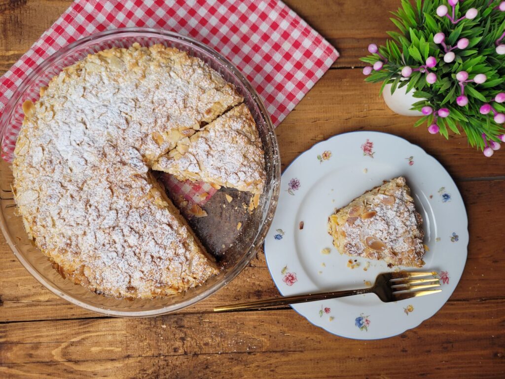Délicieux gâteau aux amandes fait maison avec du sucre en poudre et une tranche servie sur une table rustique.