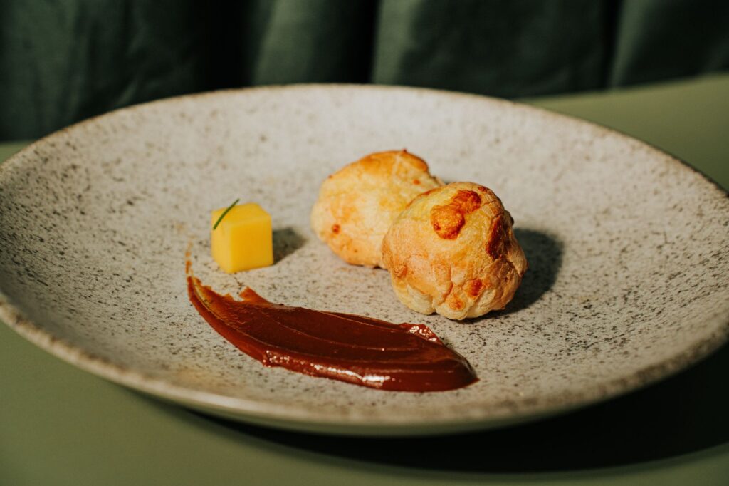 Présentation élégante de gougères avec sauce sur une assiette mouchetée, mettant en valeur la gastronomie.