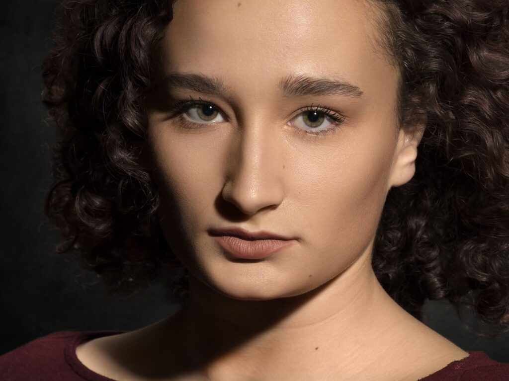 Un portrait saisissant en gros plan d'une femme aux cheveux bouclés sur fond sombre.
