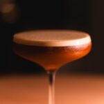 Gros plan sur un verre à cocktail contenant une boisson à plusieurs couches, dans un bar tamisé de Tokyo.