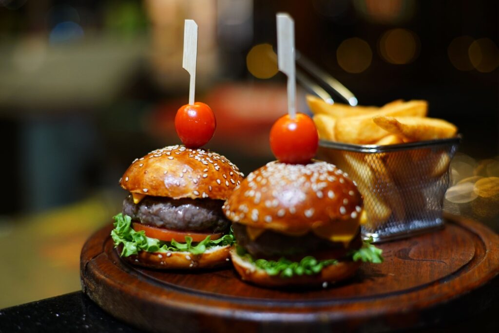 Mini-burgers gourmands avec tomates cerises et frites, servis sur un plateau en bois dans un cadre de restaurant.
