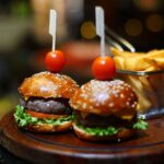 Mini-burgers gourmands avec tomates cerises et frites, servis sur un plateau en bois dans un cadre de restaurant.