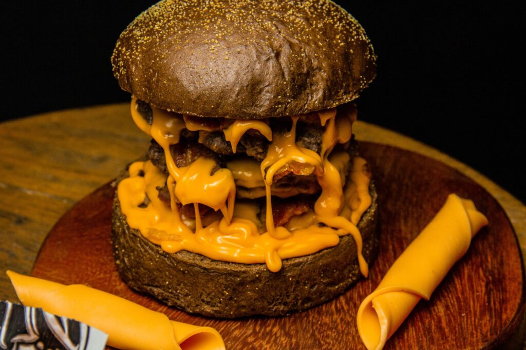 Délicieux burger gourmet avec du fromage fondu qui dégouline sur une planche en bois, parfait pour le dîner ou le déjeuner.