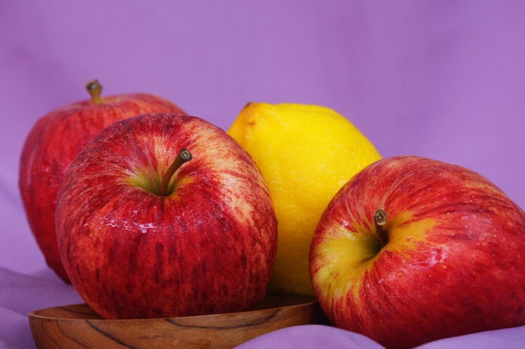 Trois pommes rouges fraîches et un citron sur un fond violet éclatant pour un contraste coloré.
