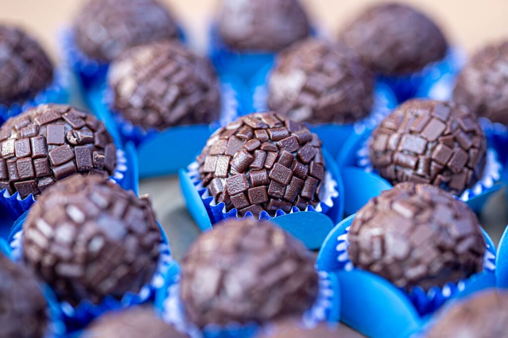 Gros plan sur des brigadeiros au chocolat à l'enrobage texturé, présentés dans des caissettes bleues, parfaits pour une douce gourmandise.