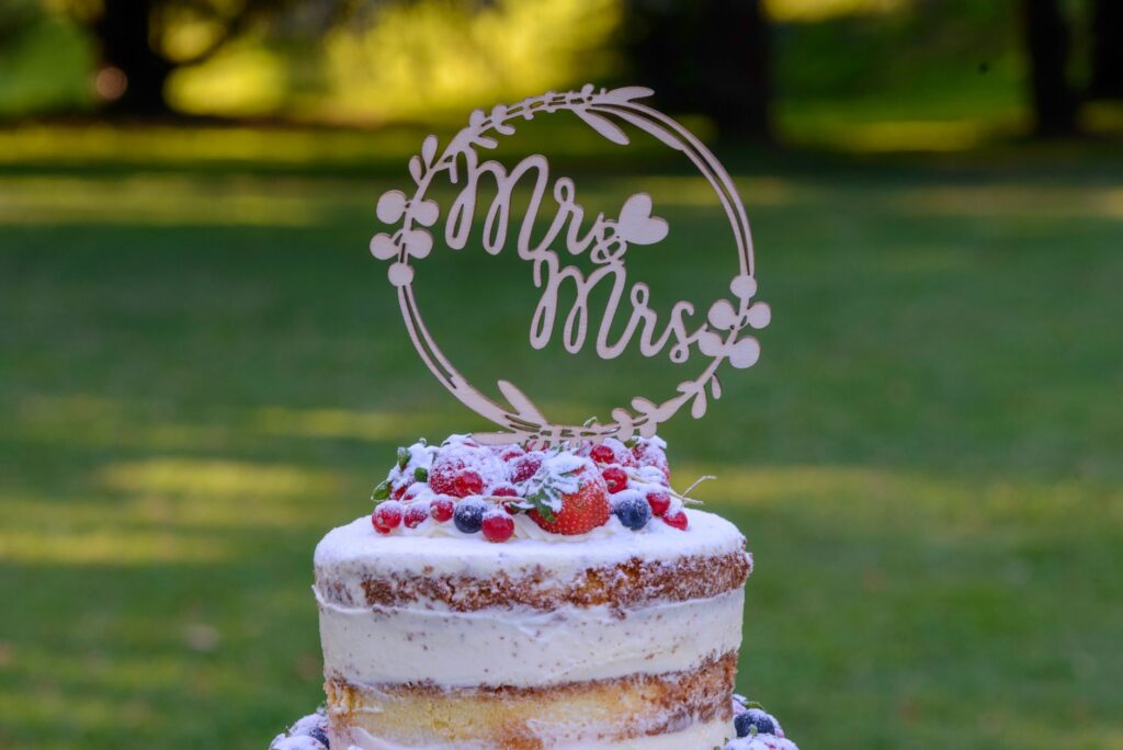 Un gâteau de mariage rustique et nu, orné de baies fraîches et d'une figurine « Mr & Mrs », dans un cadre extérieur.