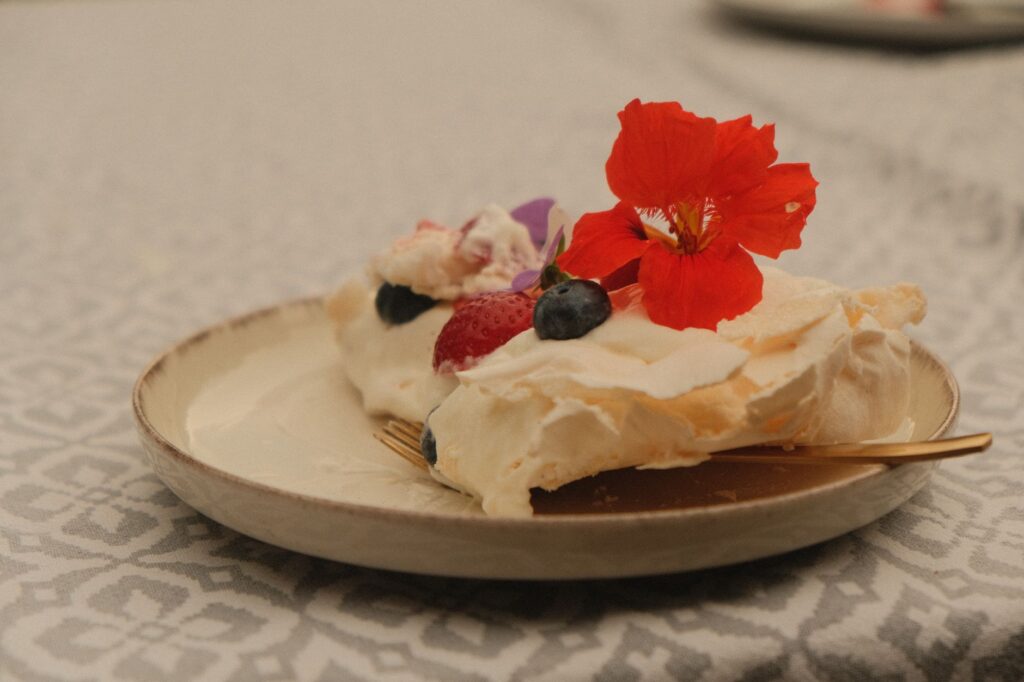 Une délicate part de dessert aux fruits rouges et aux fleurs comestibles, présentée sur une nappe à motifs.