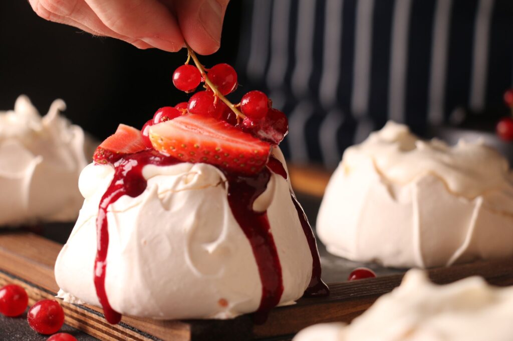 Gros plan sur une meringue garnie de fraises fraîches et de groseilles décorée à la main.