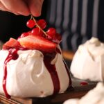 Gros plan sur une meringue garnie de fraises fraîches et de groseilles décorée à la main.