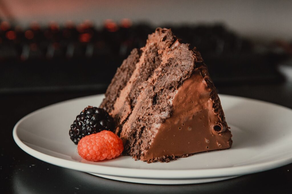 Une tranche de gâteau au chocolat riche accompagnée de framboises et de mûres fraîches sur une assiette.