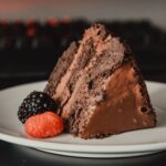 Une tranche de gâteau au chocolat riche accompagnée de framboises et de mûres fraîches sur une assiette.