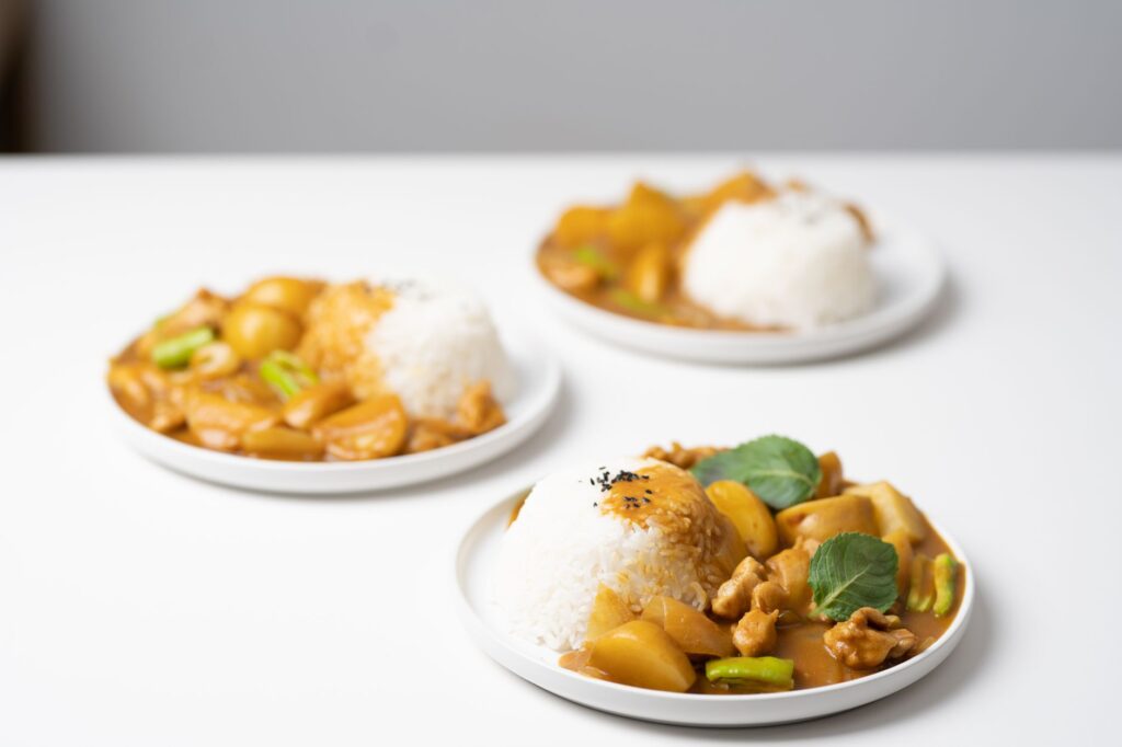 Trois assiettes de curry avec du riz, garnies de légumes, disposées sur une table blanche.