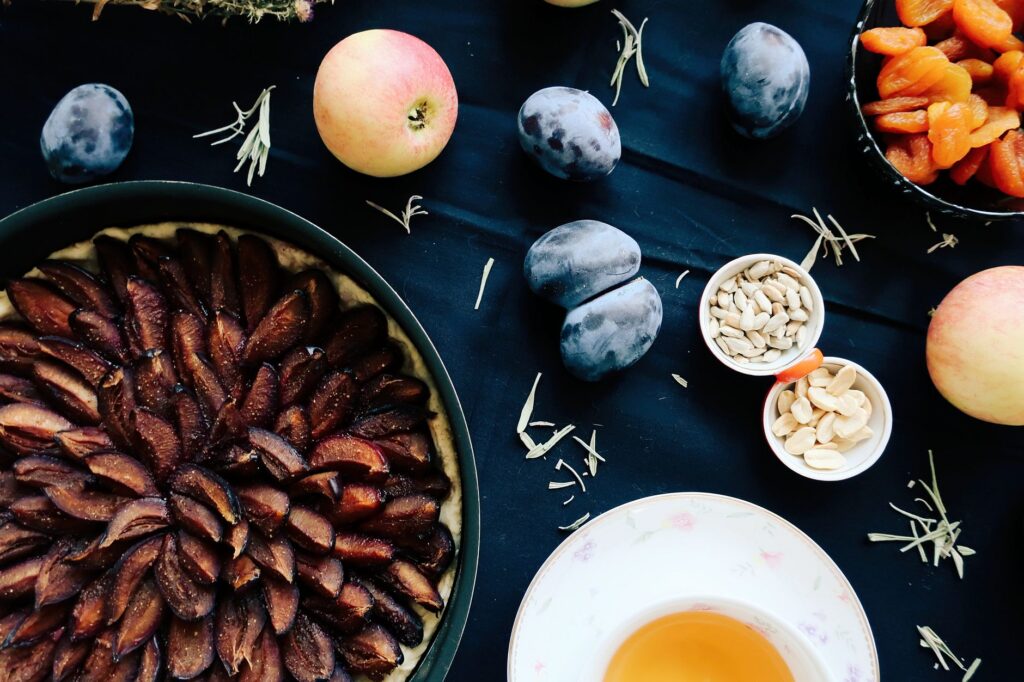 Délicieuse tarte tatin aux prunes faite maison, entourée de fruits frais et de noix.