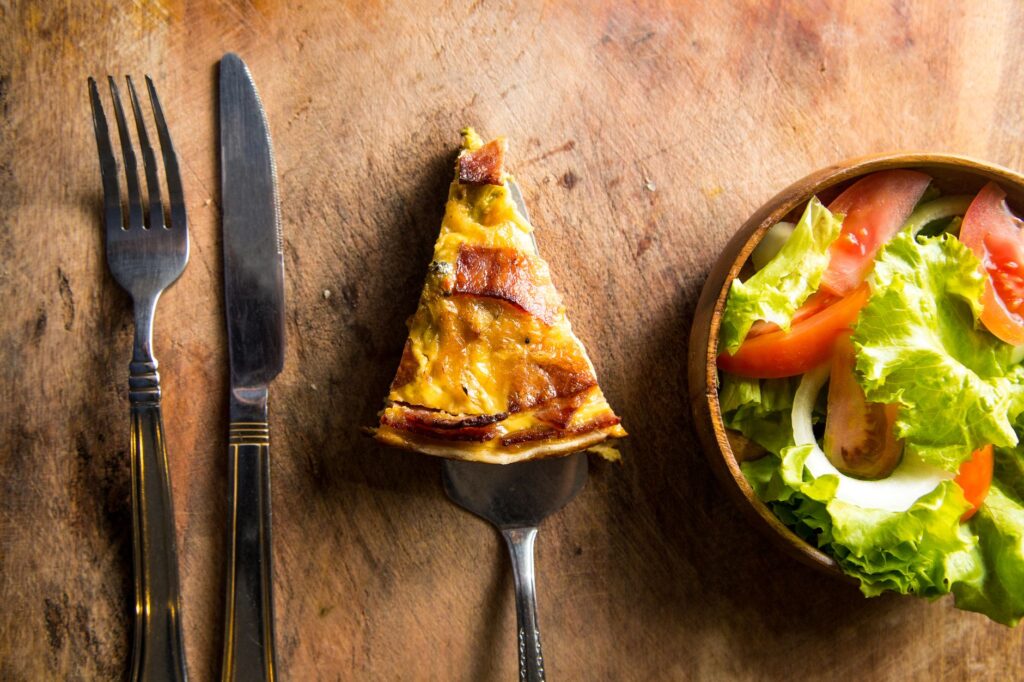 Une délicieuse part de quiche servie avec une salade de légumes frais sur une table en bois rustique.