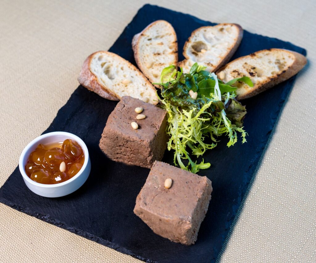 Délicieux pâté de foie avec baguette toastée, salade et chutney sur un plateau en ardoise.