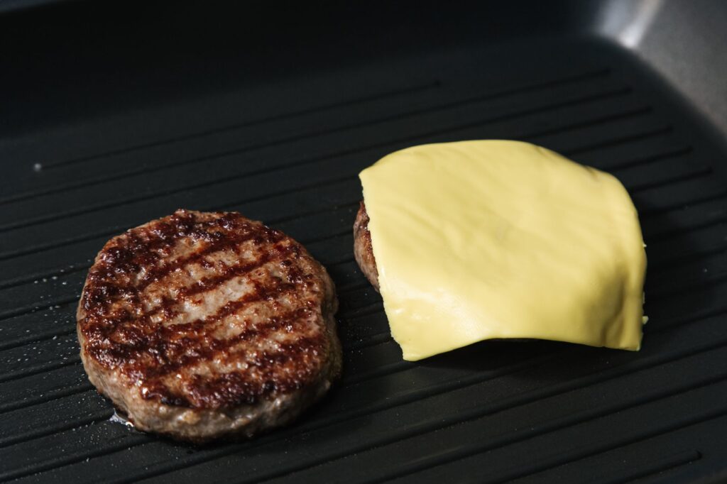 Gros plan sur des galettes de burger grillées dans une poêle, l'une recouverte de fromage fondu.