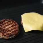 Gros plan sur des galettes de burger grillées dans une poêle, l'une recouverte de fromage fondu.