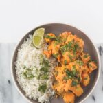 Un curry de poulet vibrant accompagné de riz basmati, garni d'herbes et de citron vert.