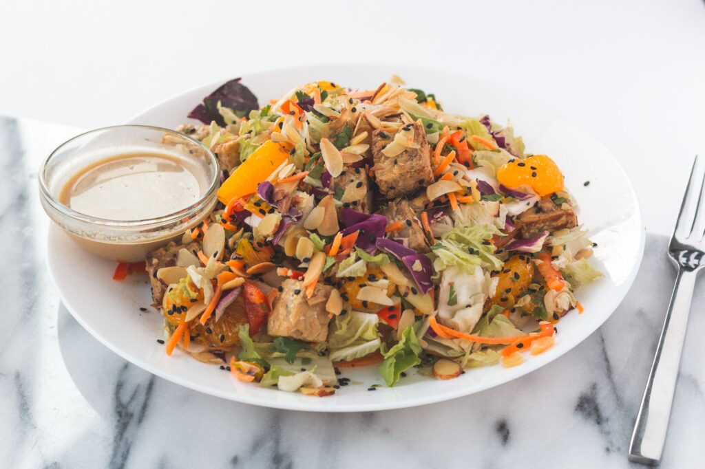 Salade de tofu fraîche et vibrante avec des tranches d'orange, des amandes et une sauce à côté.