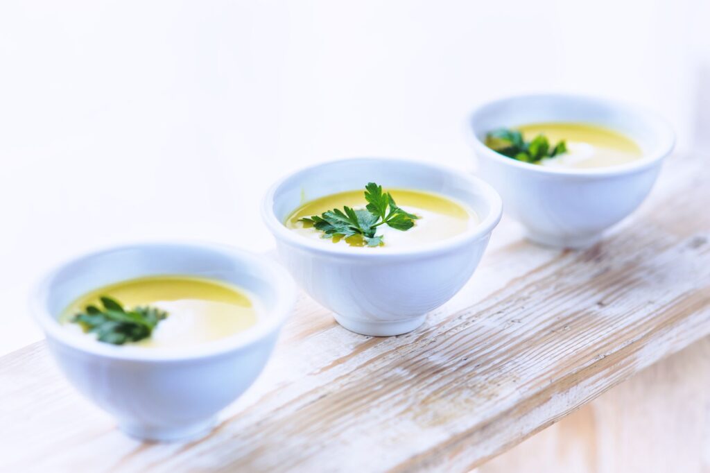 Trois bols de soupe crémeuse de panais garnie de persil frais sur une surface en bois rustique.