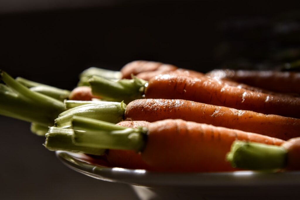 Gros plan de carottes biologiques fraîches avec des feuilles vertes dans un éclairage dramatique, mettant en avant la texture.