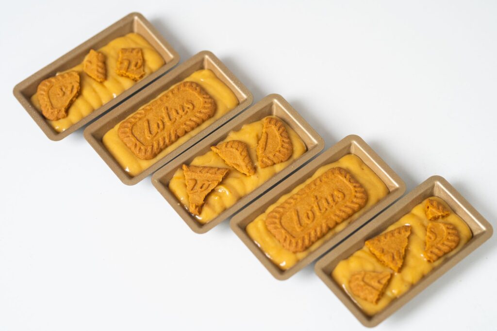 Quatre mini plateaux remplis de pâte à biscuits Biscoff prêts à cuire.