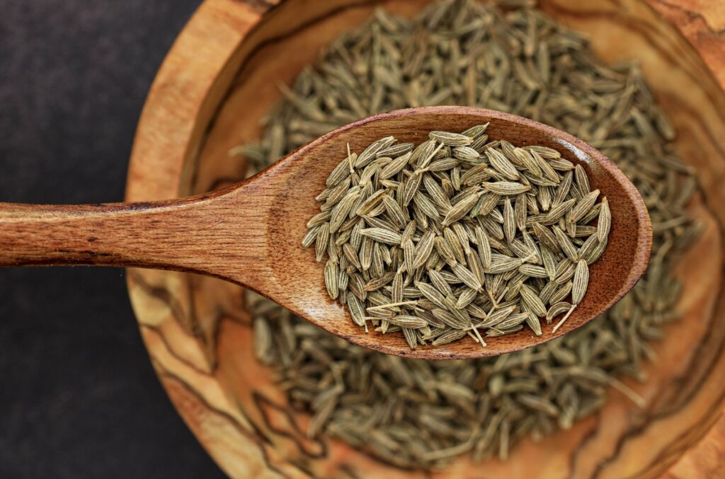 Image détaillée de graines de cumin sur une cuillère en bois pour une utilisation culinaire.