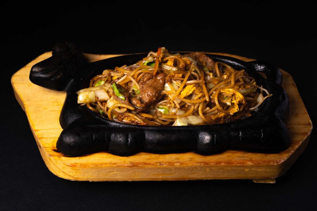 Délicieuses nouilles sautées servies chaudes sur une plaque en fonte crépitante, parfaites pour un repas savoureux.