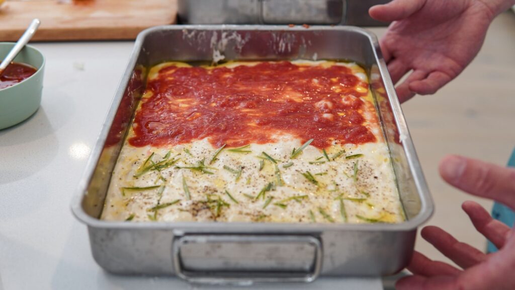 Pizza maison cuite avec des toppings de tomate et de romarin dans un plat rectangulaire.