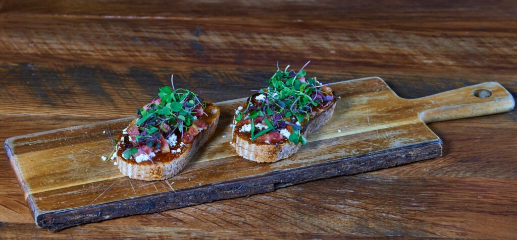 Délicieuse bruschetta garnie de micro-pousses sur une planche en bois, parfaite pour un repas gourmet.