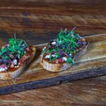 Délicieuse bruschetta garnie de micro-pousses sur une planche en bois, parfaite pour un repas gourmet.