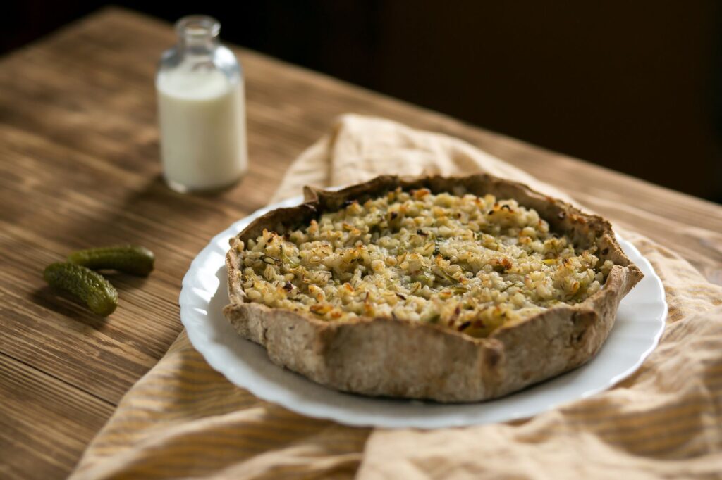 Tarte rustique chaleureuse sur une table en bois avec une bouteille de lait et des cornichons.