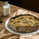 Tarte rustique chaleureuse sur une table en bois avec une bouteille de lait et des cornichons.