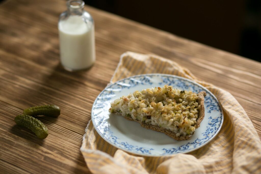 Une part de tarte rustique aux pommes de terre sur une assiette décorative avec du lait et des cornichons à proximité.