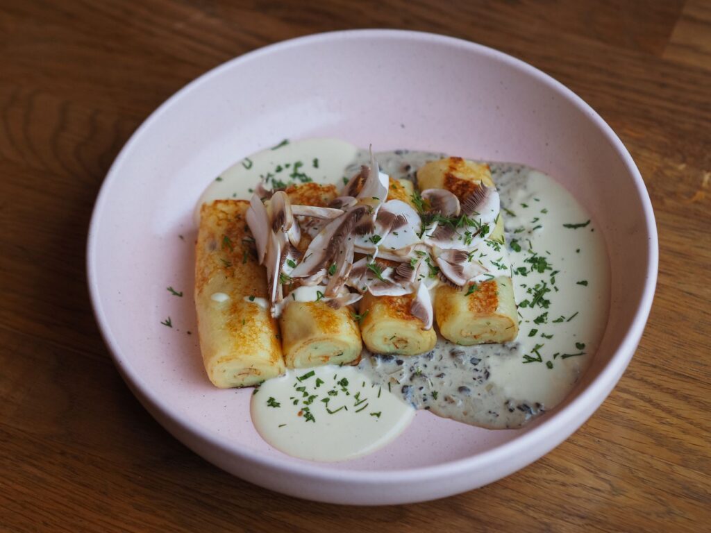 Une présentation alléchante de crêpes garnies d'une riche sauce aux champignons et d'herbes servies dans une assiette rose.