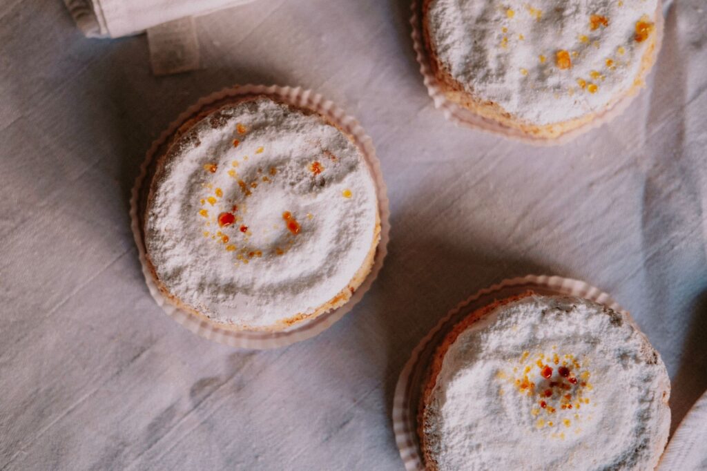 Vue en plongée de trois cupcakes saupoudrés de sucre avec des vermicelles colorés sur un tissu texturé.