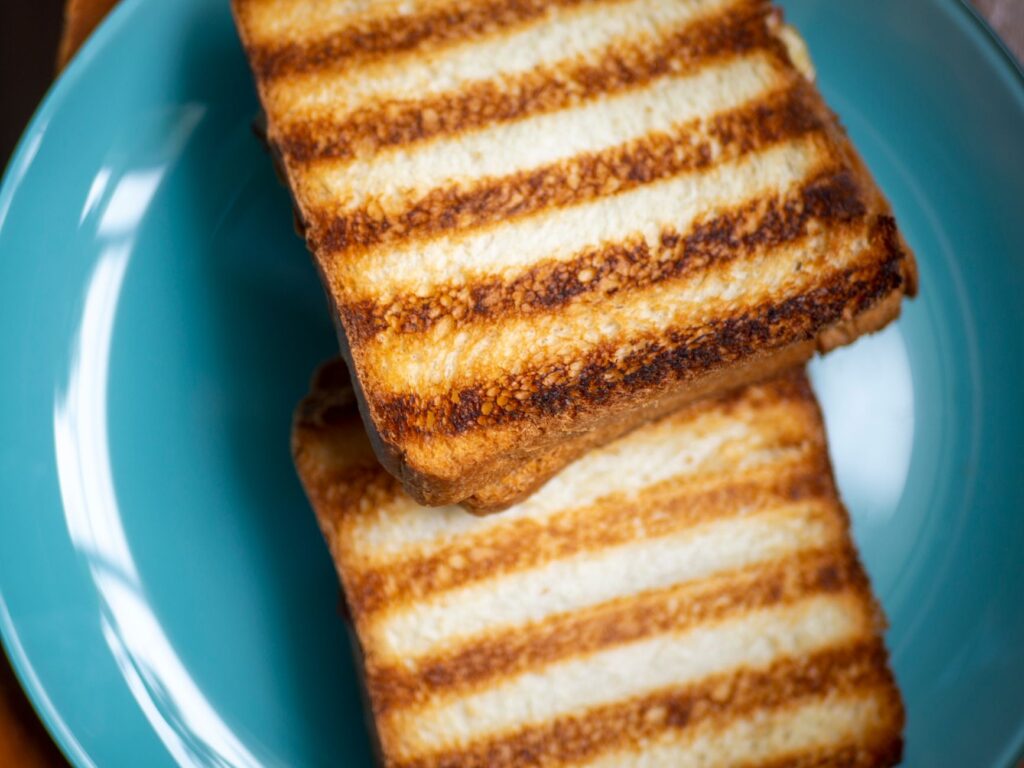 Gros plan de tranches de pain parfaitement grillées sur une assiette bleue vibrante.