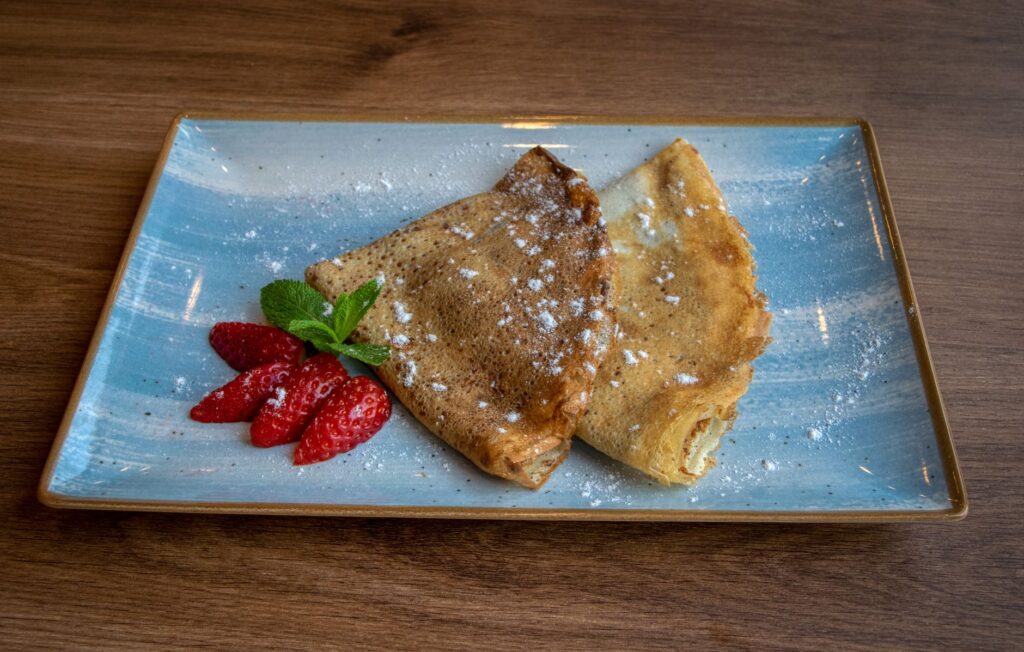 Une assiette de crêpes saupoudrées de sucre glace, servies avec des fraises et de la menthe.