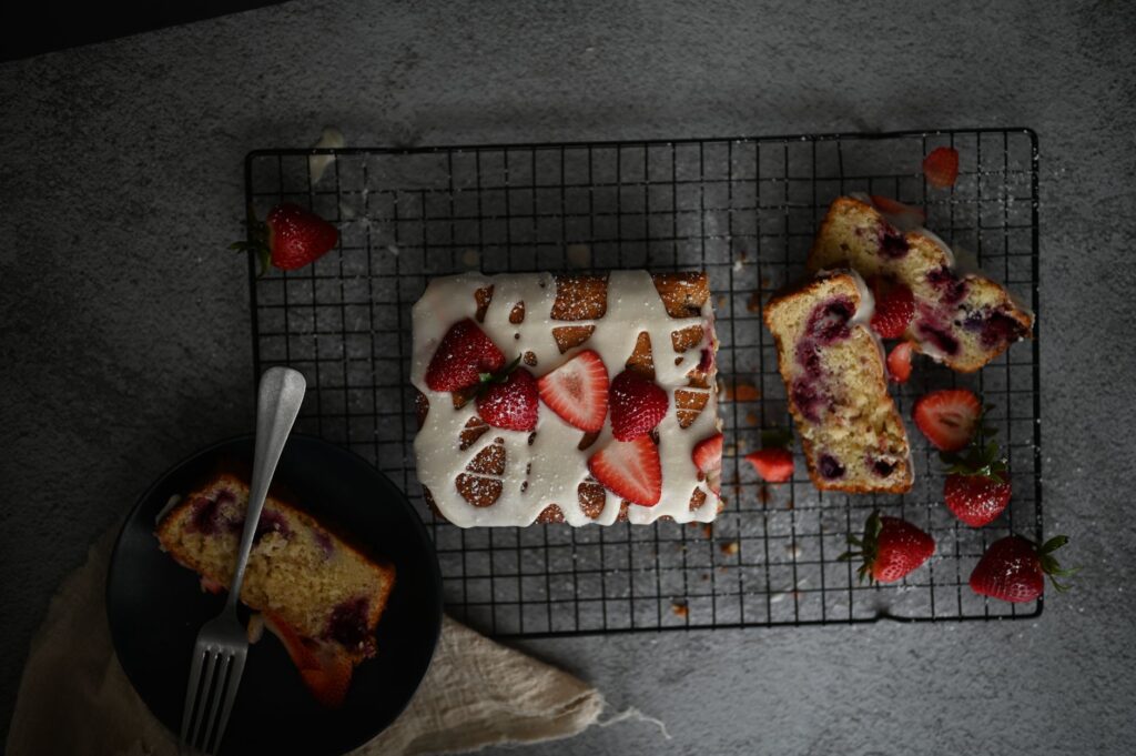 Gâteau aux fraises fraîchement cuit avec un glaçage blanc sur une grille de refroidissement, parfait pour les amateurs de desserts.
