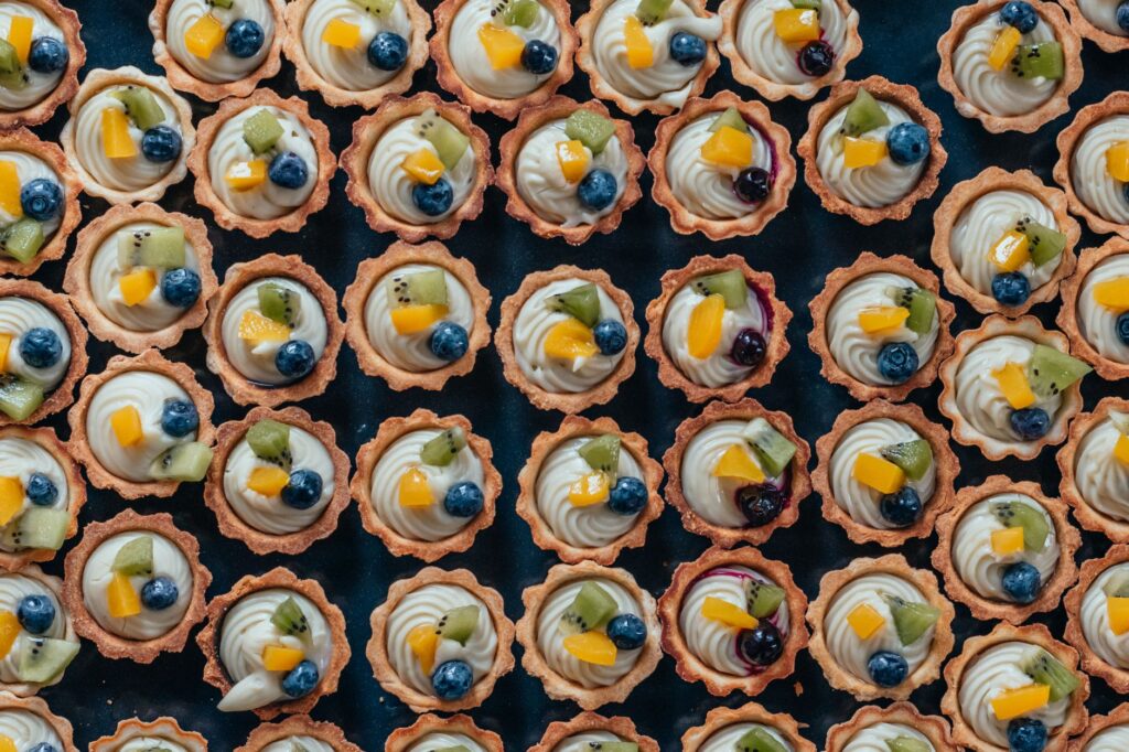 Un assortiment délicieux de mini tartes aux fruits garnies de kiwi frais, de myrtilles et de crème sur un plateau noir.