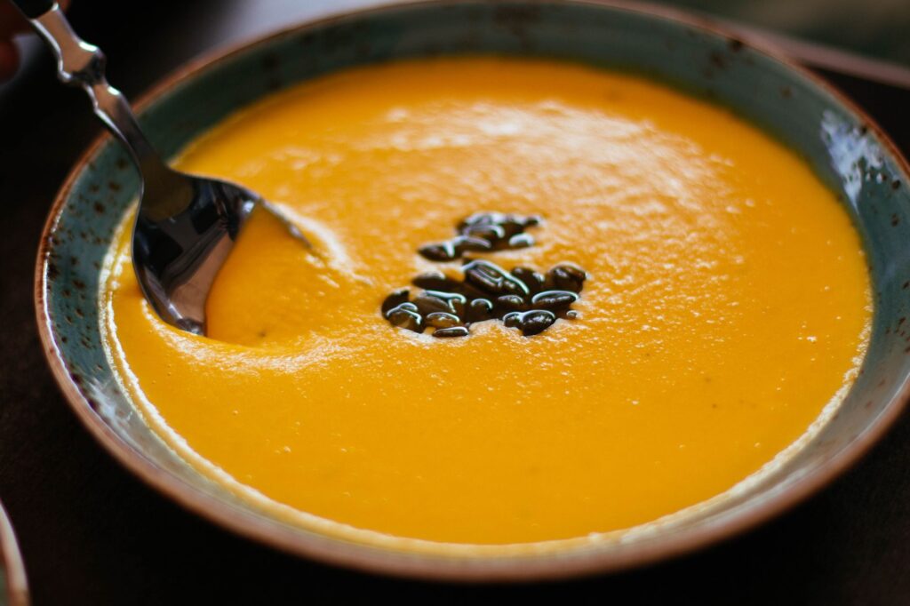 Gros plan d'une soupe de citrouille crémeuse avec des graines dans un bol en céramique bleue, parfaite pour un repas chaud d'automne.