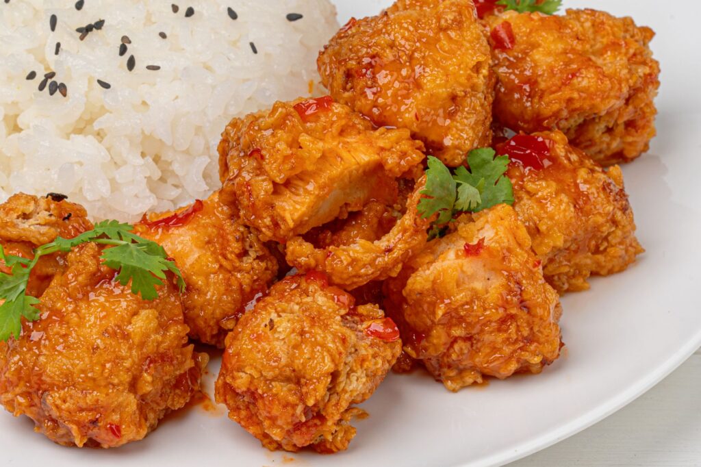 Gros plan sur du poulet croustillant épicé accompagné de riz jasmin garni de graines de sésame et de coriandre.