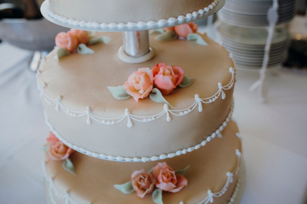 Gros plan sur un gâteau de mariage magnifiquement décoré à trois niveaux, featuring un glaçage complexe et des embellissements en rose pastel.