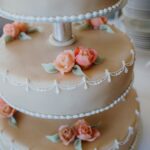 Gros plan sur un gâteau de mariage magnifiquement décoré à trois niveaux, featuring un glaçage complexe et des embellissements en rose pastel.