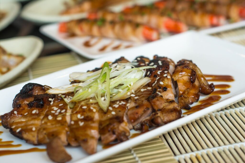 Délicieux poulet teriyaki grillé garni de poireaux frais et de graines de sésame, servi sur une assiette blanche.