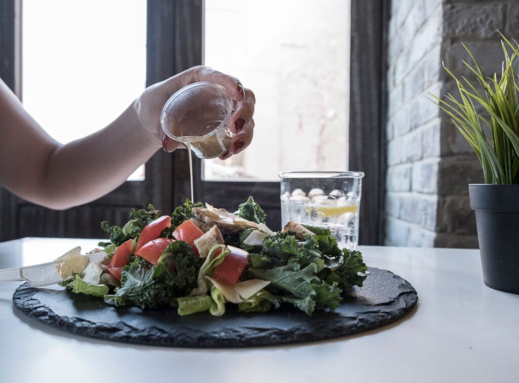Main versant une vinaigrette sur une salade fraîche avec du chou frisé et des tomates dans un restaurant moderne à Dubaï.
