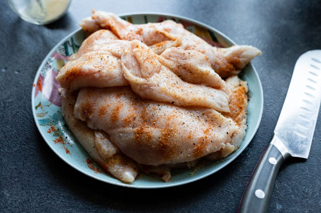 Gros plan de poitrines de poulet crues assaisonnées sur une assiette colorée à côté d'un couteau de cuisine tranchant.